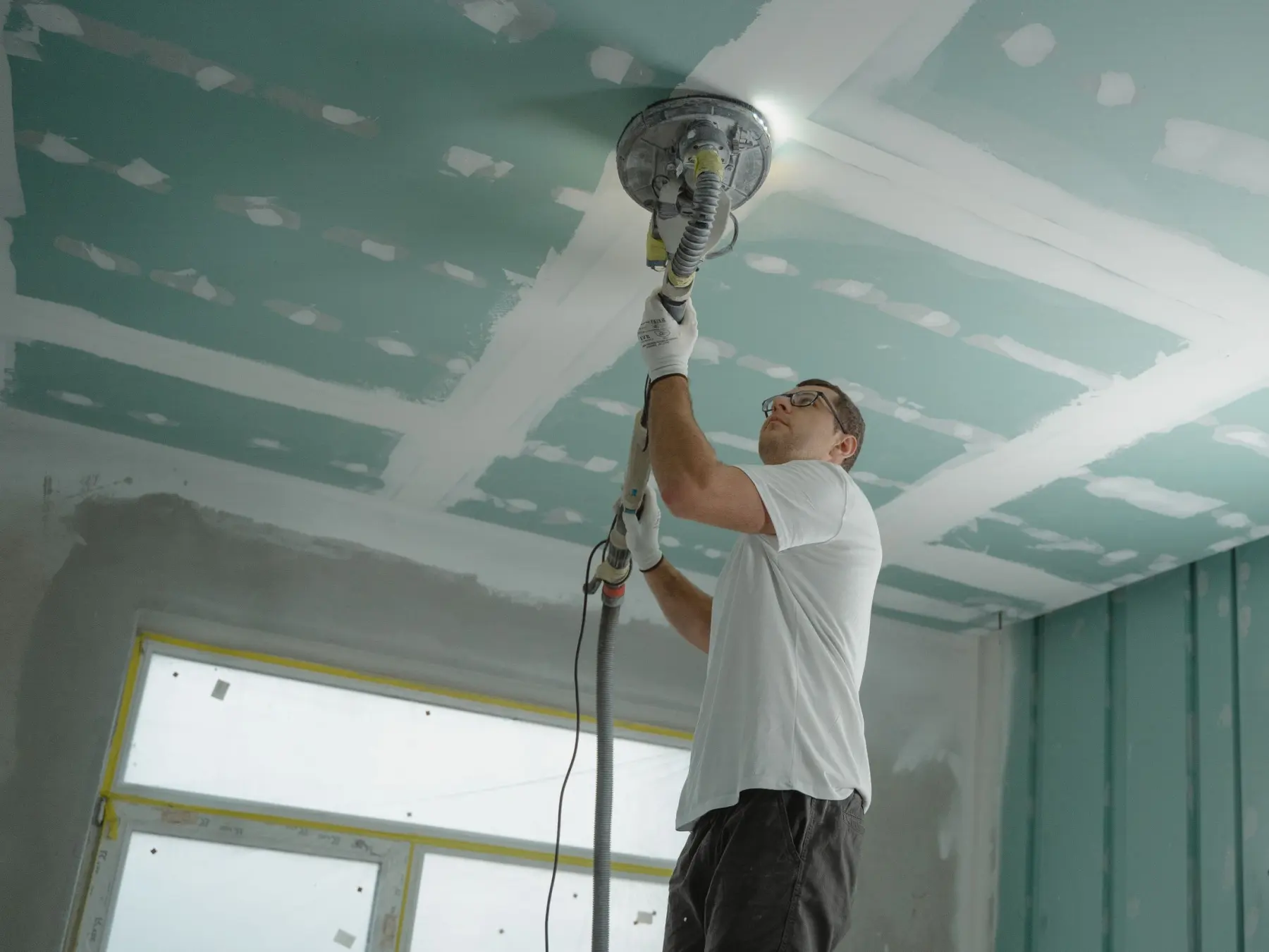 Plaquiste ponçant les joints d’un plafond en plaques de plâtre